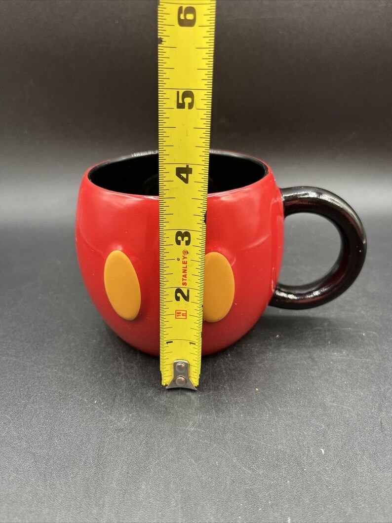 Pu&ograve; includere: Tazza in ceramica rossa con manico e interno neri, con due accenti ovali gialli. La tazza &egrave; alta circa 10 cm, simile a un personaggio dei cartoni animati.