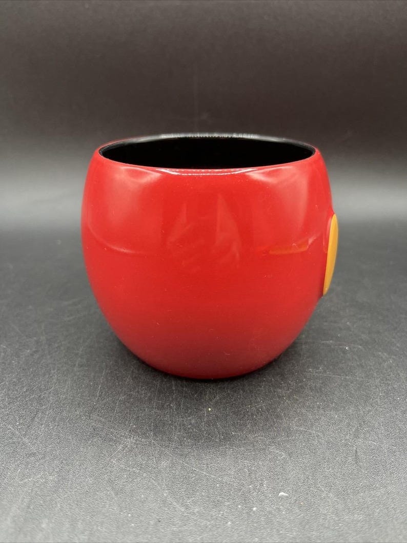 Pu&ograve; includere: Una tazza in ceramica rossa, arrotondata, con interno nero. Un piccolo accento circolare giallo &egrave; sul lato. La tazza ha una finitura liscia e lucida e un design semplice. Adatta per bevande calde o fredde. Altezza circa 10 cm.