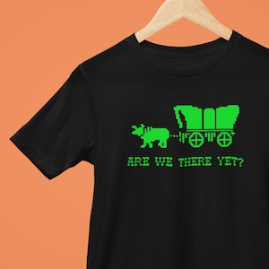 May include: Black t-shirt with a green pixelated image of a wagon pulled by an ox and the text "ARE WE THERE YET?"