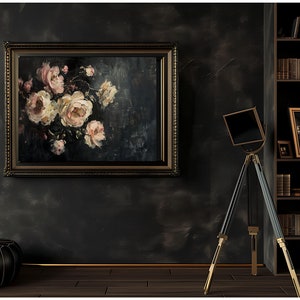 May include: An oil painting of pink and white roses in a dark, ornate frame hangs on a dark gray wall. A black and gold tripod stand with a square top is in front of the wall. A black leather ottoman sits on the wooden floor.