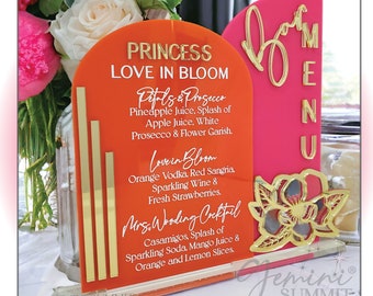 May include: Orange and pink acrylic signs with gold lettering and a gold floral design. The signs list the cocktail menu for a wedding reception. The menu includes "Petals & Prosecco", "Love in Bloom", and "Mrs. Wedding Cocktail".