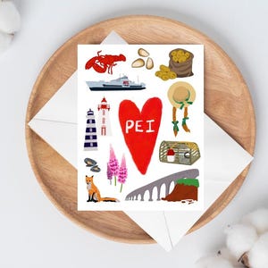 May include: A white card with colorful illustrations of a lobster, lighthouse, boat, and other images. The card has a red heart with the letters "PEI" inside. The card is on a wooden plate with a white envelope.