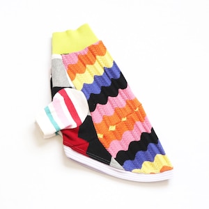 May include: A pet sweater featuring a vibrant, multi-colored wavy knit pattern in orange, pink, yellow, and blue. The garment includes a bright lime green ribbed collar, a white hem, and a single sleeve with horizontal stripes in pink, red, and teal.