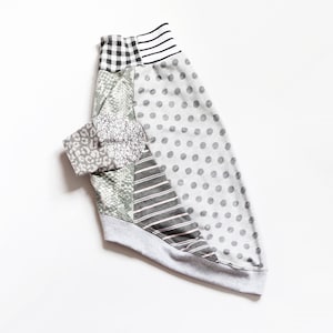 Op de afbeelding: Een shirt met lange mouwen voorzien van een patchworkontwerp met diverse patronen, waaronder grijze stippen, zwart-wit gingham, horizontale strepen, een grijze luipaardprint en een zwart-witte gebarsten textuur, met een effen grijze zoom.
