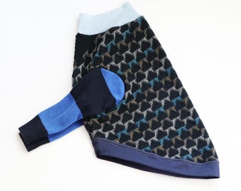 Può includere: Un maglione per animali domestici con base nera e un motivo geometrico ripetuto in bianco, blu e beige. Il capo presenta un colletto a coste azzurro, un orlo blu scuro e una manica con polsino blu scuro e una sezione azzurra.