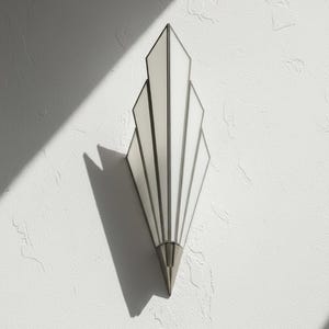 May include: A wall sconce featuring a fan-shaped design with five vertical, white frosted glass panels framed in metallic silver. The fixture tapers to a pointed, solid silver-toned base at the bottom, creating a symmetrical, elongated geometric silhouette.