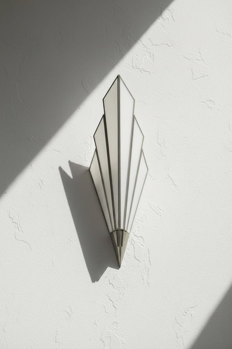 May include: A wall sconce featuring a fan-shaped design with five vertical, white frosted glass panels framed in metallic silver. The fixture tapers to a pointed, solid silver-toned base at the bottom, creating a symmetrical, elongated geometric silhouette.
