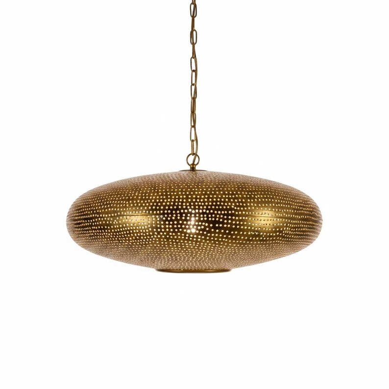 May include: A gold-toned metal pendant light fixture with a flattened, disc-like shape. The surface is covered in a dense pattern of small, circular perforations that allow light to pass through. It hangs from a matching gold-colored metal chain.