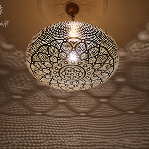 May include: A decorative, spherical pendant light fixture with intricate, geometric cut-out patterns. The light casts patterned shadows on the ceiling and walls. The fixture is suspended from a chain and emits a warm, inviting glow.