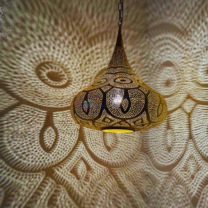 May include: A gold pendant light fixture with a geometric pattern and intricate details. The light casts a decorative shadow on the wall.