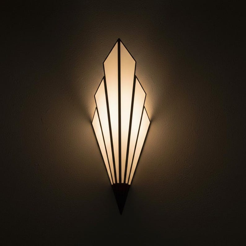 May include: A wall-mounted light fixture featuring a fan-shaped design with multiple vertical panels of frosted white glass. The panels are framed by dark, thin lines that converge at a pointed base, emitting a warm, soft glow from within.