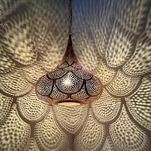 Peut inclure: Un luminaire suspendu en métal doré en forme de larme avec des motifs découpés complexes. La lumière projette un motif géométrique au plafond.