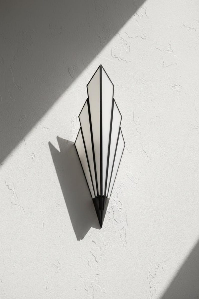 May include: A wall-mounted light fixture featuring a fan-shaped design with five vertical white glass panels framed in black metal. The fixture tapers to a pointed black metal base at the bottom, creating a symmetrical, elongated geometric silhouette.
