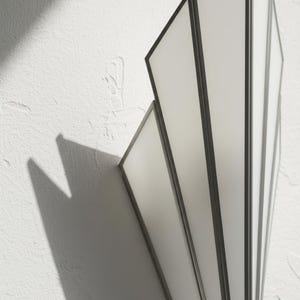 May include: A wall-mounted light fixture featuring a fan-shaped design with multiple vertical panels. The fixture is constructed with dark metal frames surrounding translucent white glass panes, creating a geometric structure that casts shadows.