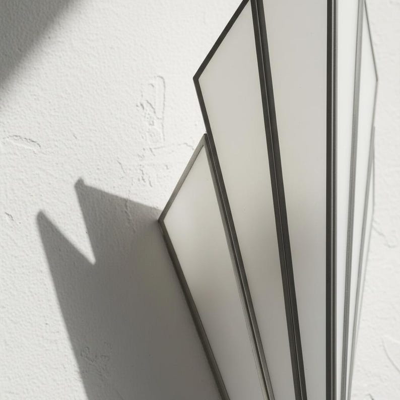 May include: A wall-mounted light fixture featuring a fan-shaped design with multiple vertical panels. The fixture is constructed with dark metal frames surrounding translucent white glass panes, creating a geometric structure that casts shadows.