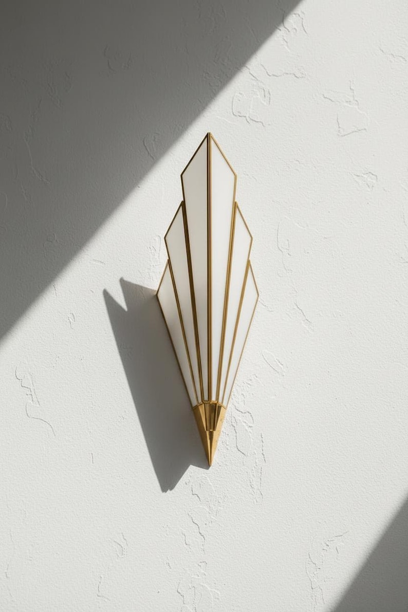 May include: A wall sconce featuring a vertical, fan-shaped design with white glass panels framed in polished gold metal. The fixture tapers to a pointed gold base at the bottom, creating a symmetrical, multi-tiered silhouette that extends outward.