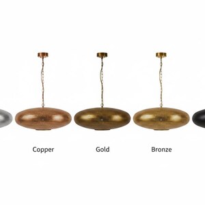 May include: Five oval-shaped pendant lights hanging from chains, each featuring a textured metallic finish. The colors from left to right are silver, copper, gold, bronze, and black. Each lamp has a matching circular ceiling canopy.