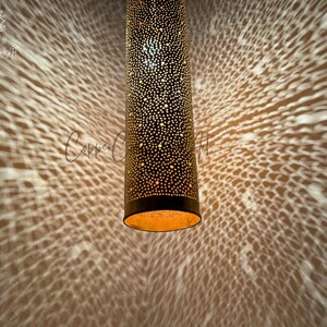 May include: A gold metal pendant light fixture with a cylindrical shape and a perforated design. The light casts a pattern of small circles on the wall behind it.