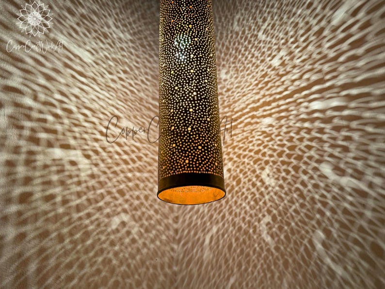 May include: A gold metal pendant light fixture with a cylindrical shape and a perforated design. The light casts a pattern of small circles on the wall behind it.