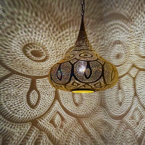 May include: A gold-toned metal pendant light fixture with intricate cut-out designs. The light casts a patterned shadow on the wall behind it.
