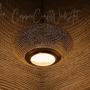 May include: A round, dark-toned metal pendant light fixture featuring a dense pattern of small, perforated holes that emit a warm, glowing light. The fixture is suspended by a chain and displays the text CopperCraftWorkArt in the upper area.