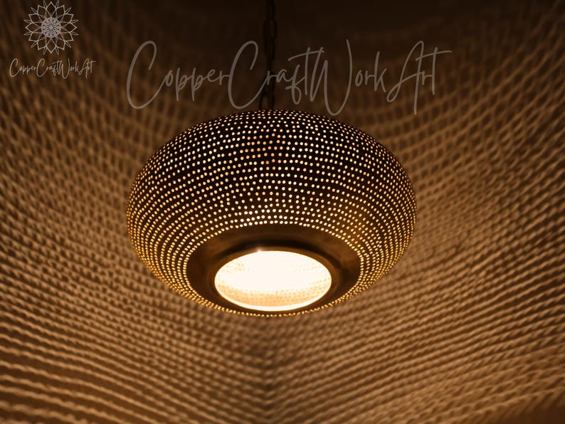 May include: A round, dark-toned metal pendant light fixture featuring a dense pattern of small, perforated holes that emit a warm, glowing light. The fixture is suspended by a chain and displays the text CopperCraftWorkArt in the upper area.