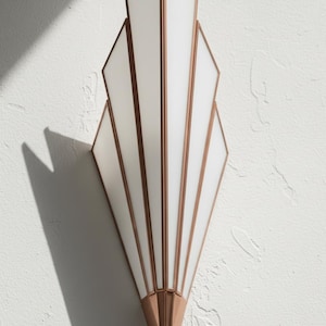 May include: A wall sconce featuring a fan-shaped design with white frosted glass panels framed in metallic copper. The fixture has a vertical, symmetrical structure with multiple segments that taper toward the bottom, creating a geometric appearance.