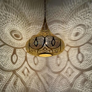 May include: A gold Moroccan pendant light with intricate cut-out designs casts a patterned shadow on the ceiling.