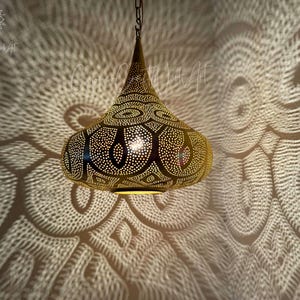 May include: A gold pendant light fixture with a geometric pattern. The light fixture is hanging from a chain and casts intricate shadows on the wall.
