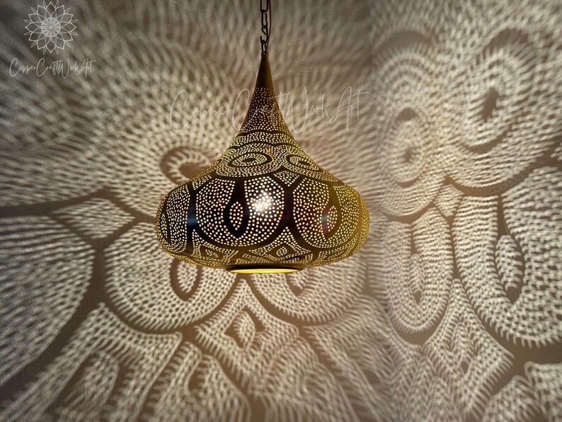 May include: A gold pendant light fixture with a geometric pattern. The light fixture is hanging from a chain and casts intricate shadows on the wall.