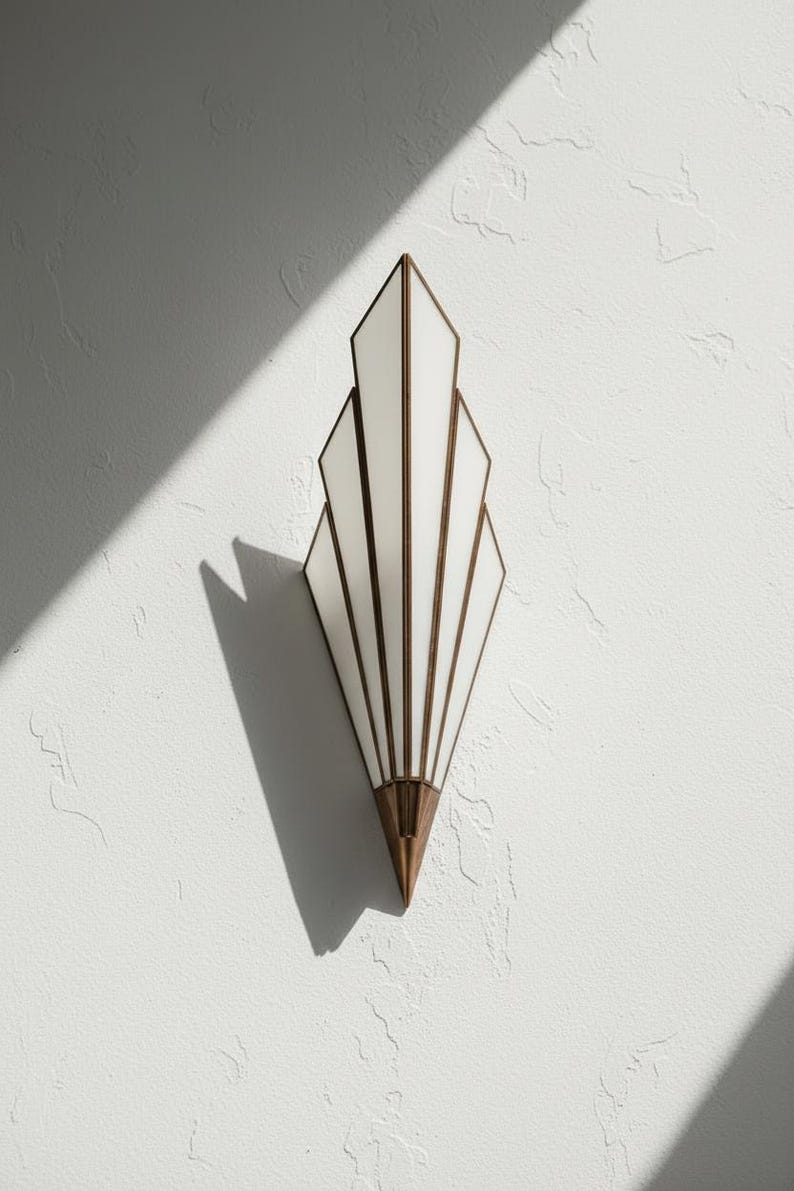 May include: A wall sconce featuring a fan-shaped design with five white glass panels framed in metallic bronze. The fixture tapers to a pointed bronze base at the bottom, creating a geometric silhouette that extends vertically against the wall surface.