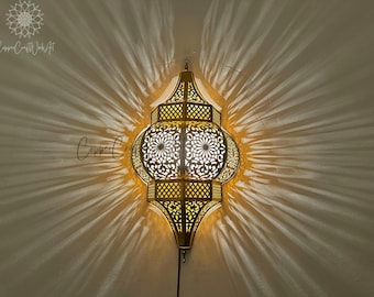 May include: A gold metal Moroccan-style pendant light fixture with intricate cut-out designs. The light fixture is hanging from the ceiling and casting a shadow on the wall.