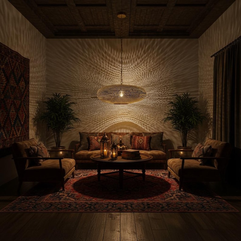 May include: A large, oval-shaped, metallic pendant light fixture with a textured, perforated surface hangs from the ceiling, casting intricate, radiating light patterns across the walls of a dimly lit room with two armchairs and a sofa.