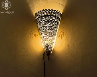 May include: A decorative wall sconce with a metal, intricate, cut-out design. The sconce is lit and casts a warm glow on the wall.