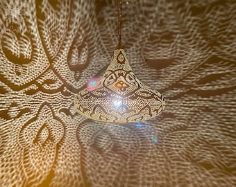 Puede incluir: Una lámpara colgante de metal dorado con un patrón decorativo intrincado. La luz proyecta un patrón geométrico en el techo.