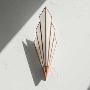 May include: A wall-mounted light fixture featuring a fan-shaped design with five white glass panels framed in copper-toned metal. The structure tapers to a pointed base, creating a geometric silhouette that extends outward from the mounting point.