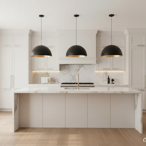 Puede incluir: Tres lámparas colgantes de cúpula en negro mate con interiores en oro metálico suspendidas sobre una isla de cocina de mármol blanco. La cocina cuenta con gabinetes blancos, un salpicadero de mármol y suelo de madera clara.