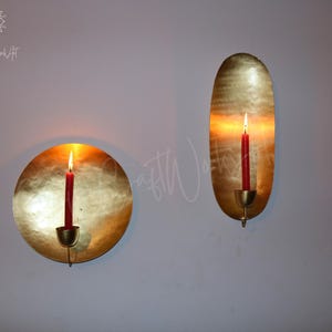 May include: Two gold metal candle holders with a round and oval shape. Each holder has a red candle inside.