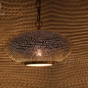 May include: A dome-shaped pendant light fixture crafted from metallic material with a perforated surface pattern. The lamp features a warm, glowing light emitting from the bottom opening and through the small holes, suspended by a metal chain.