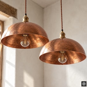 Peut inclure: Deux suspensions en forme de dôme avec une finition en cuivre martelé. Chaque luminaire est suspendu par un cordon en tissu marron torsadé et comprend une douille en métal doré contenant une ampoule transparente de style Edison.