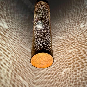 May include: A gold metal lampshade with a perforated pattern casts a decorative shadow on the ceiling. The lampshade is cylindrical and has a warm, inviting glow.