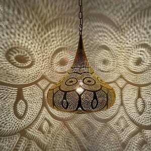 May include: A gold-toned pendant light fixture with a geometric design. The light casts intricate shadows on the wall behind it.