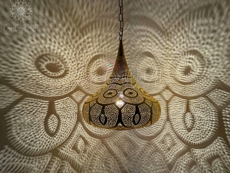May include: A gold-toned pendant light fixture with a geometric design. The light casts intricate shadows on the wall behind it.