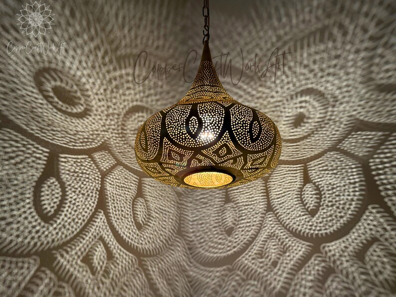 May include: A gold Moroccan pendant light with intricate cut-out designs casts a patterned shadow on the ceiling.