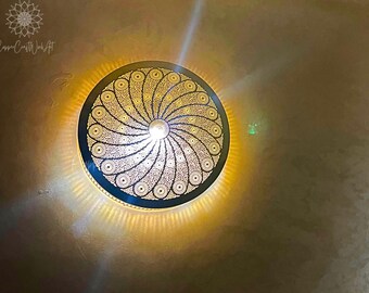 May include: A round, gold-colored ceiling light fixture with a decorative, intricate, circular pattern. The light is on and casting a warm glow.