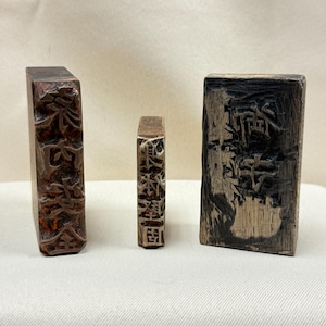 Könnte beinhalten: Drei antike Holzstempel mit geschnitzten asiatischen Schriftzeichen. Die Stempel sind rechteckig und unterschiedlich groß, mit dunkelbraunen und rotbraunen Farbtönen. Die Schnitzereien sind aufwendig und detailliert.