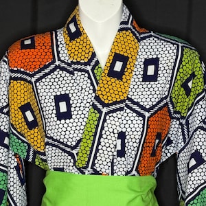 May include: A colorful kimono-style top with a geometric pattern in orange, yellow, green, and white. The top has a V-neck and long sleeves. A bright green sash wraps around the waist. The fabric is patterned with small white circles and dark blue lines.