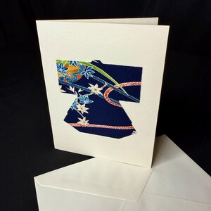 Könnte beinhalten: Eine weiße Karte mit einem ausgeschnittenen Kimono aus blauem und weißem Stoff. Der Kimono hat ein Blumenmuster mit roten und goldenen Akzenten.