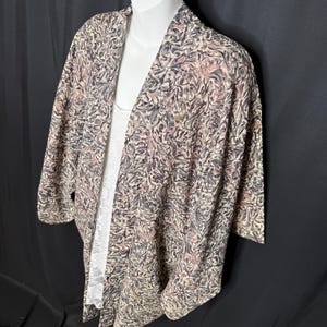 May include: A patterned kimono-style jacket in beige, gray, and pink. The jacket has a flowing design and three-quarter sleeves. A white top is visible underneath. The fabric has a swirling, abstract pattern.