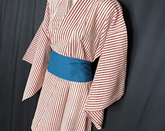 Op de afbeelding: Een traditionele Japanse yukata-robe met verticale rode strepen op een crèmekleurige achtergrond. De robe heeft wijde mouwen en wordt in de taille vastgemaakt met een tealblauwe obi-riem. Het kledingstuk wordt op een mannequin gepresenteerd.